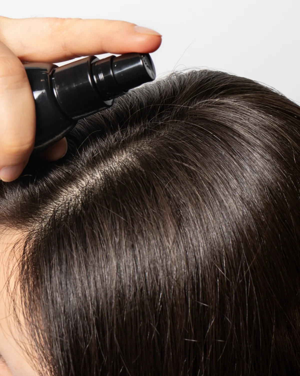 Aplicación de un producto con pulverizador sobre el cuero cabelludo, con el cabello separado por la raya.