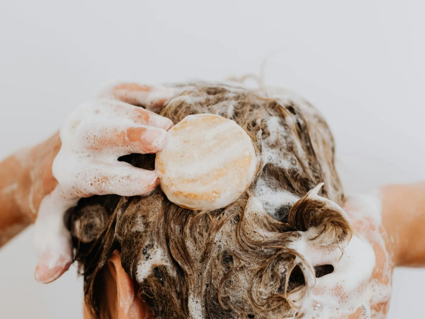 Manos masajeando el cabello con abundante espuma durante el lavado.